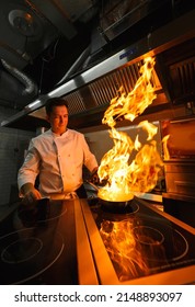 Close-up Of The Chef's Hands Cooking Food On Fire. The Chef Burns Food In A Professional Kitchen