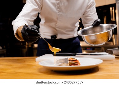 close-up of a chef's hands holding a bowl and pouring sauce from a spoon onto the finished dish - Powered by Shutterstock