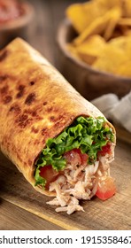 Closeup of a chicken burrito with lettuce and tomato on a wooden cutting board