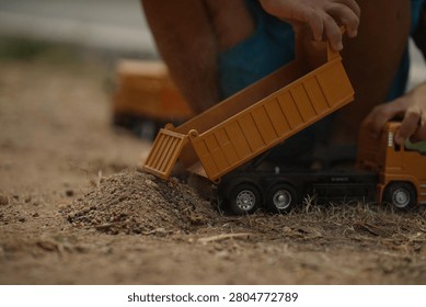 Close-up of a child loading dirt into a yellow toy dump truck with their hands