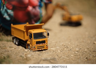 Close-up of a child loading dirt into a yellow toy dump truck with their hands.