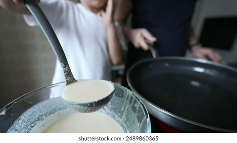 Close-up of child pouring pancake batter into pan, kitchen activity, child focused on task, parent assisting, white t-shirt, morning light, home environment, making breakfast together - Powered by Shutterstock