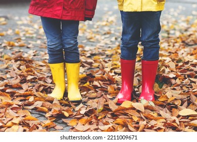 Closeup Of Children In Red And Yellow Rubber Boots In Autumn Park In Colorful Rain Coats And Clothes. Close-up Of Kids Legs In Shoes Dancing And Walking Through Fall Autumnal Leaves And Foliage.