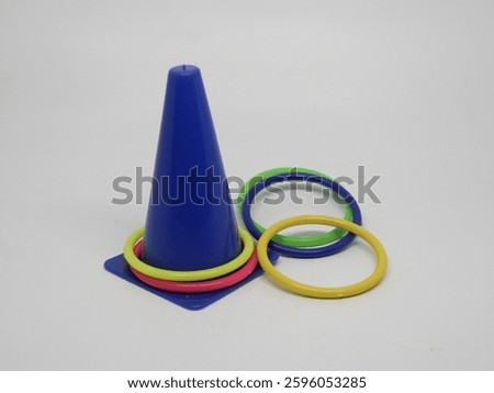 Close-up of a children's ring toss game featuring a blue plastic cone on a square base, with yellow, green, and pink rings scattered around it, isolated on a clean white background.