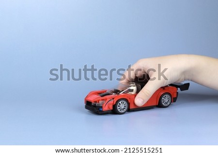 Close-up of a child's hand playing with a miniature car from the constructor on a blue background. Copy space