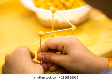 close-up of a child's hands assembling a geometric figure with toothpicks and corn kernels