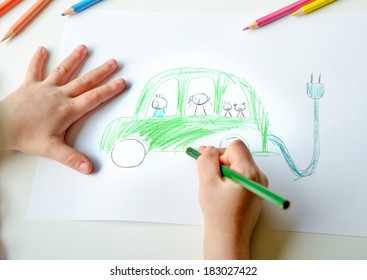 Close-up Of Childs Hands Drawing A Green Electric Zero Emission Car