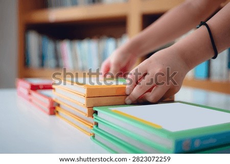 Close-up of a child's hands organizing and stacking colorful books neatly on a table in a library or classroom. Education, reading habits, and organization concept for stock photography.