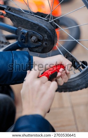 Close-up of a child's hands using a red hand pump to inflate a flat bicycle tire, showing repair and self-reliance outdoors