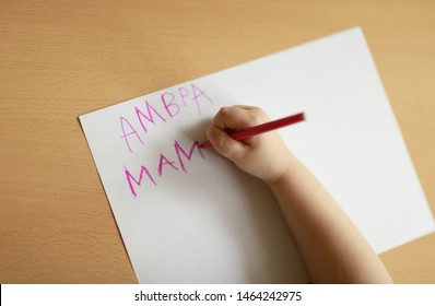 Closeup of child's hands writing letters on a paper sitting at the table