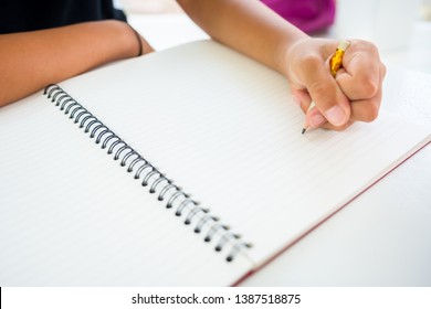 Closeup Child's Left Hand With Short Pencil Going To Start Writing Or Drawing Something In The Opened Notebook