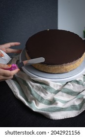 Closeup Chocolate Cheesecake On Cakeboard On Lazy Susan Dark Mood With Hand Using Spatula To Smooth Cake