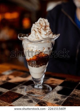 Close-up of a chocolate and vanilla ice cream with chantilly in a glass cup on a restaurant table. Dark background