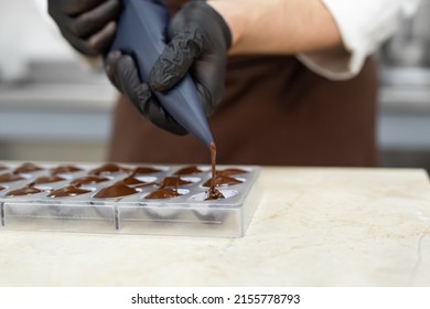 Close-up of the chocolatier's hands pouring chocolate into the molds. The chef's pastry bag pours hot melted chocolate into a silicone mold. - Shutterstock ID 2155778793
