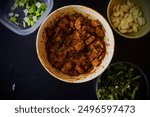 Close-up of Choila, a traditional Nepali Newari dish, accompanied by fresh ingredients. The spiced and marinated meat is presented in a bowl, with chopped green onions, garlic cloves, and leafy greens