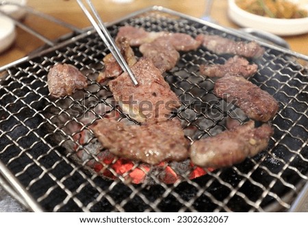 Close-up of chopstick and Korean beef with prime rib on the grill and charcoal fire in the restaurant, South Korea
