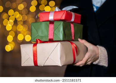 Close-up of Christmas gift boxes in women's hands. Woman with gifts on the background of a festive glowing garland on the street. Christmas and New Year's shopping, concept of holidays.Selective focus - Powered by Shutterstock