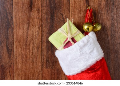 Closeup of a Christmas stocking filled with presents hanging from a hook on a wood wall. Two jingle bells also hang from the hook in horizontal format. - Powered by Shutterstock