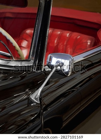 Close-up of chrome side mirror and white steering wheel.  A classic 1950s roadster. The interior is finished in high-quality red leather. Selective focus.