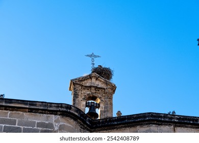 Close-up of a church bell tower with a clock and a stork nest, featuring stone details and a blue sky. - Powered by Shutterstock