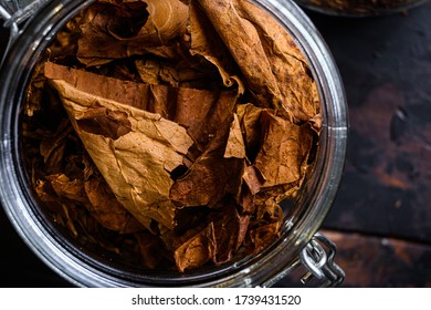 Close-up Cigar And Pile Of Tobacco Leaves Of Dried Tobacco In Glass Jars On Rustic Wood Dark Table Top View Overhead