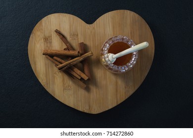 Close-up of cinnamon sticks and honey on heart shaped chopping board - Powered by Shutterstock