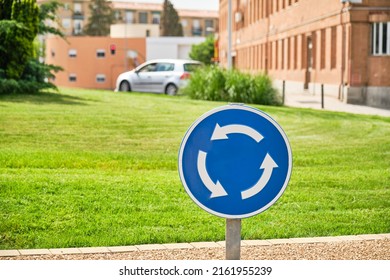 close-up of a circular blue traffic sign for mandatory traffic on a grassy roundabout with buildings in the background