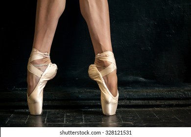 Close-up classic ballerina's legs in pointes on the black wooden floor 