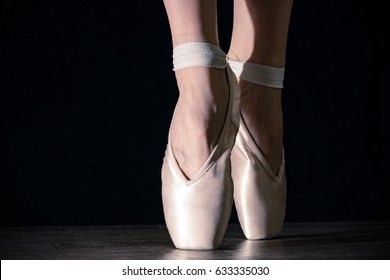 Close-up classic ballerina's legs in pointes on the black background and wooden grey floor