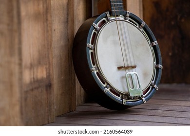 Close-up of a classic Banjo-Mandolin body, leaning against wood paneling, on decking. 