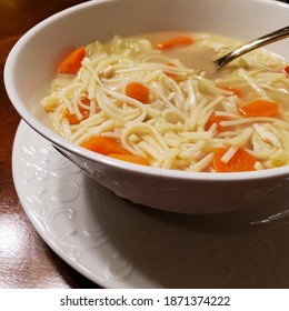 Closeup Of Classic Chicken Noodle Soup In White Bowl And Saucer With Dark Wood