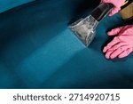 Closeup of cleaner in pink gloves using wet vacuum extractor to wash sofa seat, showing deep upholstery cleaning and stain removal service.