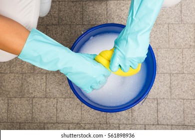 Close-up Of Cleaner Woman Hand Squeezing Cloth In Bucket Filled With Soap Sud - Powered by Shutterstock