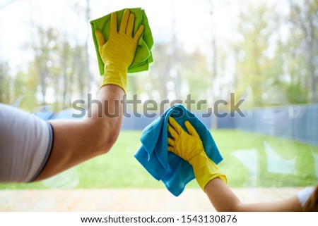 Closeup of cleaners holding rags, wearing yellow rubber gloves. Cleaning glass of window