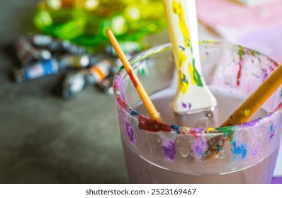 Close-up of a clear container filled with vibrant paint and brushes, showcasing an artist's workspace, perfect for illustrating creativity and artistic expression. - Powered by Shutterstock