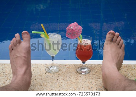 Closeup of cocktails and male's feet at the edge of the outdoor swimming pool
