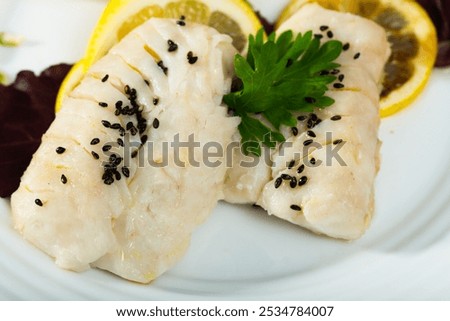 Closeup of codfish steamed and served with herbs and lemon at plate