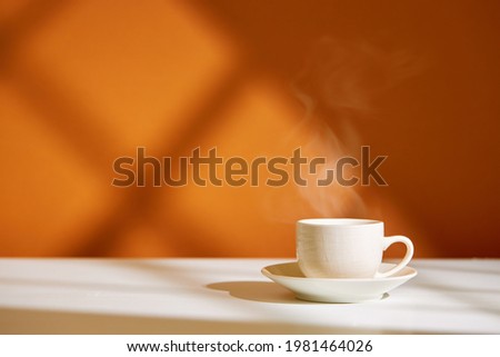 Close-up of coffee cup on table at direct sunlight. Morning coffee with steam in white cup.