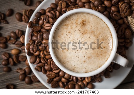 Close-up of coffee cup with roasted coffee beans on wooden background. View from top 