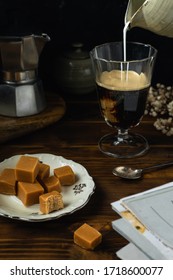 Close-up Of Coffee Glass With Some Salted Caramel Fudge, Moka Coffee Maker On Dark Wooden Table