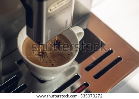 Close-up of coffee pouring from coffee machine into white cup at restaurant, bar or pub. Professional coffee brewing. Coffee break concept. Old fashioned sepia colors.