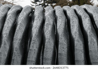 A close-up of a coil of high-voltage electrical cable covered in raindrops. The black insulated wires glisten with moisture, emphasizing their texture and durability