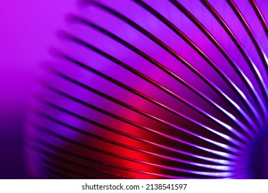 Closeup of coiled metal spring with sufficiently high strength and elastic properties in neon purple and pink light. Macro photo, selective focus. - Powered by Shutterstock