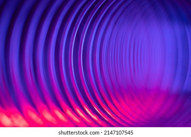 Closeup of coiled metal spring with sufficiently high strength and elastic properties in neon blue and pink light. Macro photo, selective soft focus. Abstract shot.