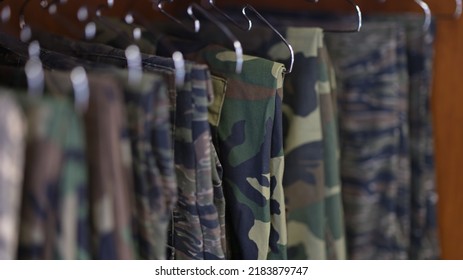 Close-up of collection of military uniform trousers in wardrobe. Camouflage military clothes concept
