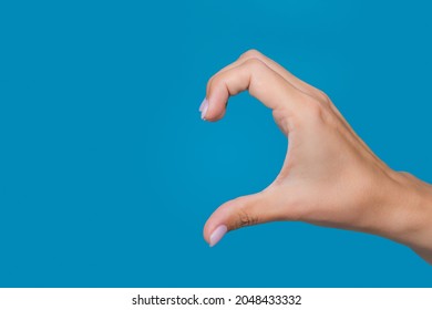 Close-up color photography of female caucasian hand isolated on blue background. Young adult woman forming shape of half of heart with her fingers. Point of view shot with copy space