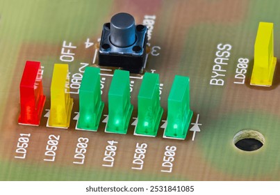 Closeup of colored LED lights and black button on beige printed circuit board. Green, yellow or red rectangular light-emitting diodes and pushbutton switch on PCB detail. Active electronic components.
