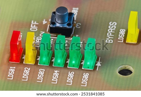 Closeup of colored LED lights and black button on beige printed circuit board. Green, yellow or red rectangular light-emitting diodes and pushbutton switch on PCB detail. Active electronic components.