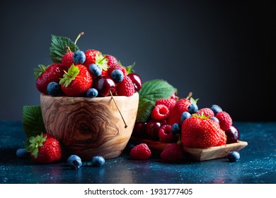 A close-up colorful assorted mix of strawberry, blueberry, raspberry, and sweet cherry in a studio on a dark blue background. - Powered by Shutterstock