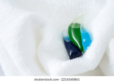 Closeup Of Colorful Laundry Eco Detergent Capsule Pod On Fresh Fluffy Fabric Or Terry Towel, White Background